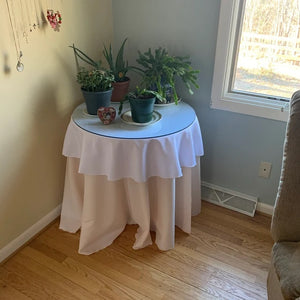 Polyester linens on a round table layered sitting a corner of a home by a window with plants