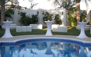 White Spandex table covers on cocktail tables outdoors by a pool with seating in the background