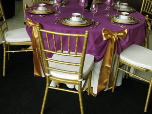 Layered wedding linens in white and aubergine with gold banquet chairs and bows 