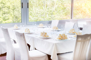 White corporate linens with matching chair covers and Ivory napkins on plates by a window