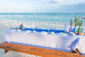 Beautiful white Poly linens on a rectangular table with  plates on the beach