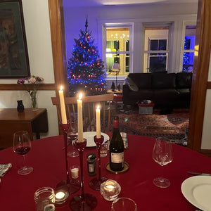 Holiday dinner setting with red round tablecloth with candelabra, wine glasses and bottle