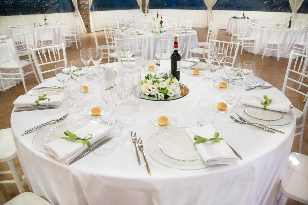 Poly premier round table linens in a wedding reception with place settings and flower centerpiece