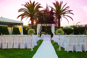 White wedding aisle runner leading to alter with chairs on either side and palm trees