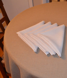 White Havana napkins layered on top of a table with a natural-colored tablecloth on a round table