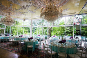Fine cotton linens on round tables in a luxurious wedding reception with giant chandeliers above