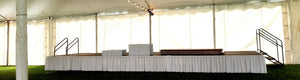 White shirred pleat skirt on stage during reception set up with flat tables and chairs under a tent 
