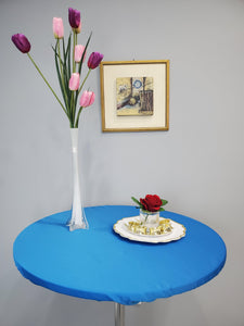 Blue round fitted tablecloth with elastic on a cocktail table with a vase of flowers