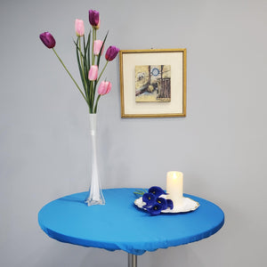 Blue round fitted tablecloth, candle and white vase with purple tulips