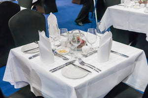 White poly tablecloths with matching napkins standing on a table with silverware