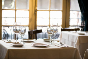 Tan table linens at a restaurant with matching napkins, plates, and drinkware by a window view