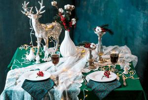 Green table cloth on a Holiday Display table at a show with plates, napkins and a reindeer statuette
