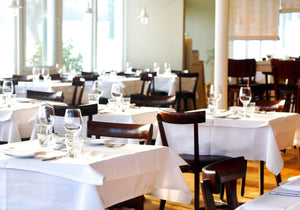 White restaurant linens layered on square tables with napkins and wine glasses