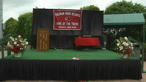 Graduation stage with a black skirt in an outdoor ceremony with flowers and a podium