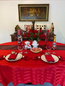 Red oval tablecloth with dinner napkins and red roses on the table
