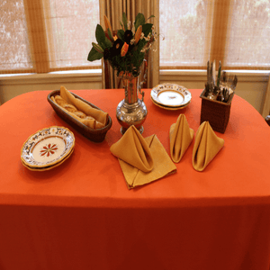 Rectangular orange formal linens on a small serving station table with bread and flowers on it