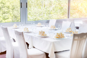 White table linens in a banquet restaurant setting with clam folded napkins on plates by a window