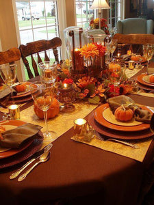 Brick colored table linens with a gold runner and matching placemats and Thanksgiving decorations