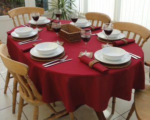  red oval table linen with red napkins, red wine, and china set on the table