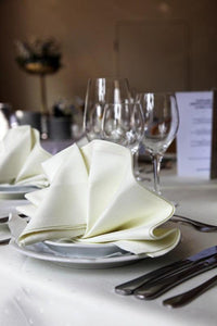 Vanilla colored fine linens on a restaurant table with napkins folded clam style on plates