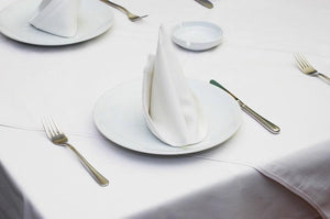 Formal white linens layered on table with standing napkins on plates and an ash tray