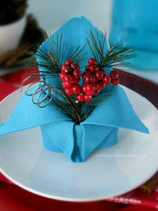 blue linen napkin folded with holiday greenery set on a white plate at a table setting