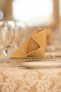 Rows of beige linen folded napkins on glass plates at dinner setting