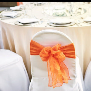 Ivory-colored wedding linens with white chair covers and orange chair ties in a bow