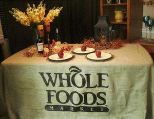 Custom printed BUrlap tablecloth for Whole Foods with plates and flowers on top