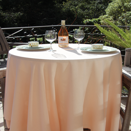 Ivory-colored tablecloth on a round table with plates and wine glasses