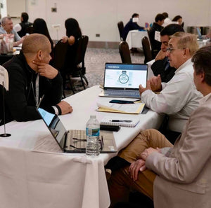 Trade show attendees at a learning booth. TGable has a white blank tablecloth