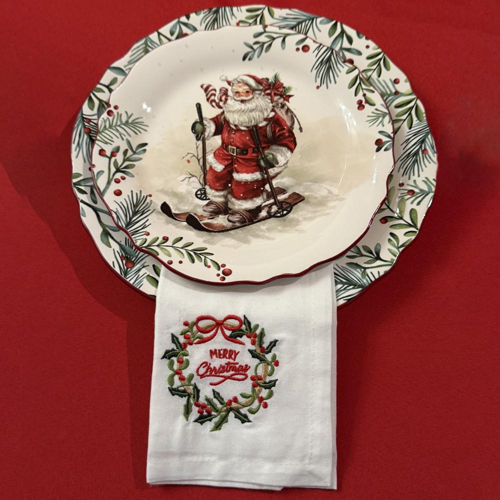 White dinner napkin embroidered Merry Christmas on holiday china with Santa Clause.