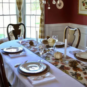 Dining table set for a meal with fall-themed decor, including pumpkins and leaves on a tablecloth.