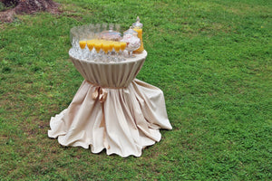 Our Ice Peach wedding linens dress a refreshments table outdoors with orange juice on top.