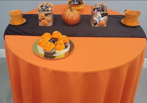 An Orange tablecloth on a round table with a black velvet runner and Halloween treats on top