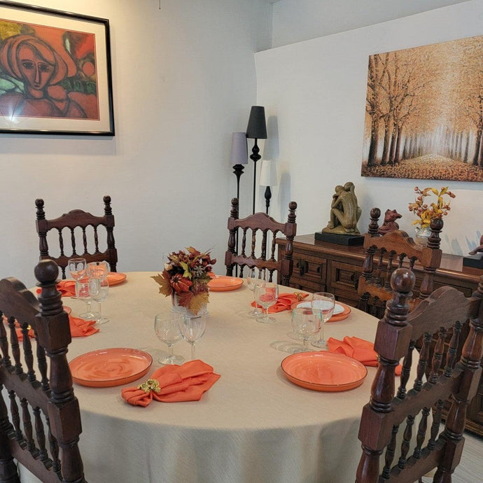 Dining room table with an oal tablecloth in tn orange dinner napkins and plates. Lots of fall decoration.