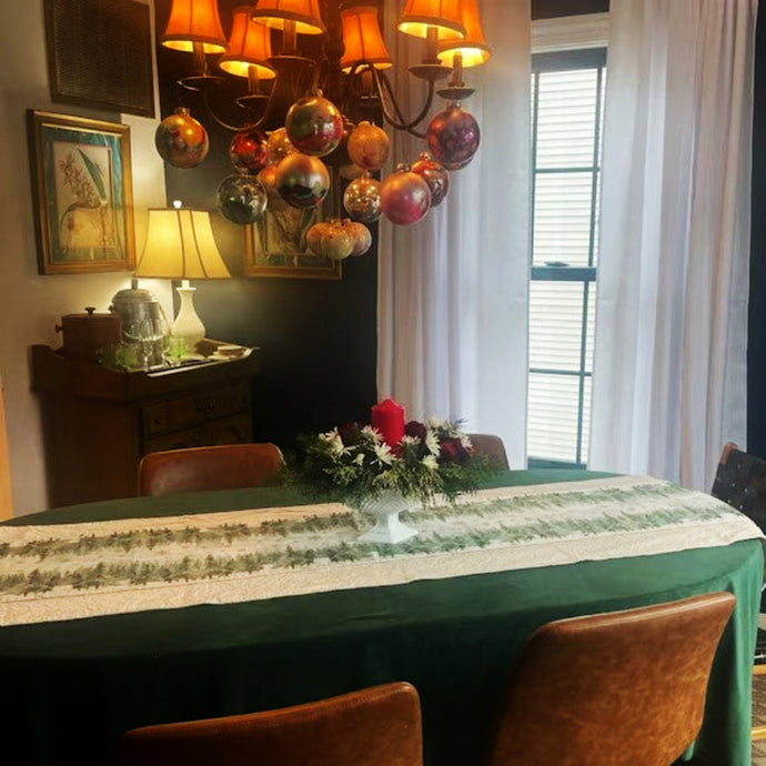 Dining room with a table set for a meal, decorated with a green velvet tablecloth, velvet table runner  and floral centerpiece.