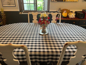 black and white checkered tablecloth on a farmhouse table with a silver tray, flower vase and flowes ontop; of the oval tablecloth.