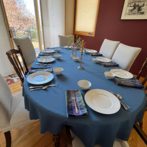 Blue oval tablecloth on a large wooden table. Very elegant table linen with china and candles on the tablescape