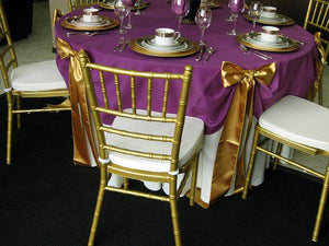 Layered wedding tablecloths with golden chairs and bows. 