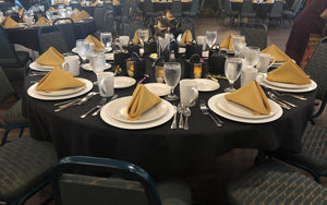 Black Table linens on round tables with gold napkins folded into triangles on top of plates
