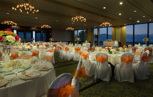 Lavish reception with white table linens and orange chair sashes with mountains in the background