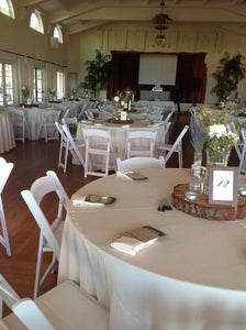 Ivory-colored table covers with matching folded napkins and wooden centerpiece