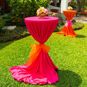 Beautiful pink and orange linens on cocktail tables set up outdoors with sashes tied in the center