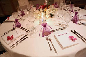 Soft white linens at reception with purple gift baggies