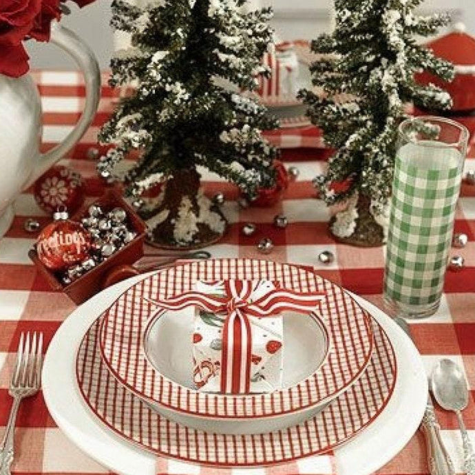 Christmas-themed table setting with red and white checkered tablecloth, decorative trees, and festive place settings.