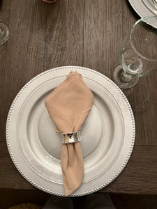 Silver napkin ring holder with a dinner napkin on top f a charger plate and china.