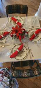 Holiday red napkins rolled in a silver napkin ring holder on a table set for Christmas celebration.