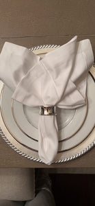 White napkin folded on a silver napkin ring with a beige background