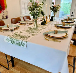 Rectangular white tablecloth with a floral table runner, dinner napkins and beautiful china and floral arrangement in a dining room in a home.